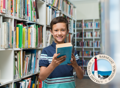 Elementary school male student holding a book in a library in front of bookcase for Fast ForWord case study success story of Barnegat Township Elementary School in New Jersey