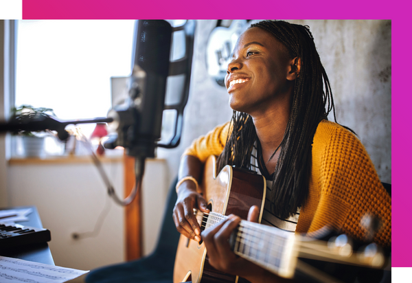 A Black female musician is smiling while strumming a guitar