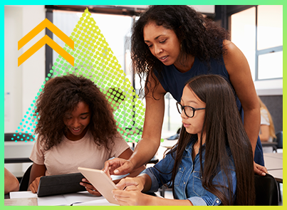 A teacher standing up helping a sitting student with a problem on the student's tablet.